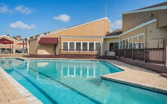 A swimming pool located in a residential area featuring surrounding buildings, wooden deck, and lounge chairs.