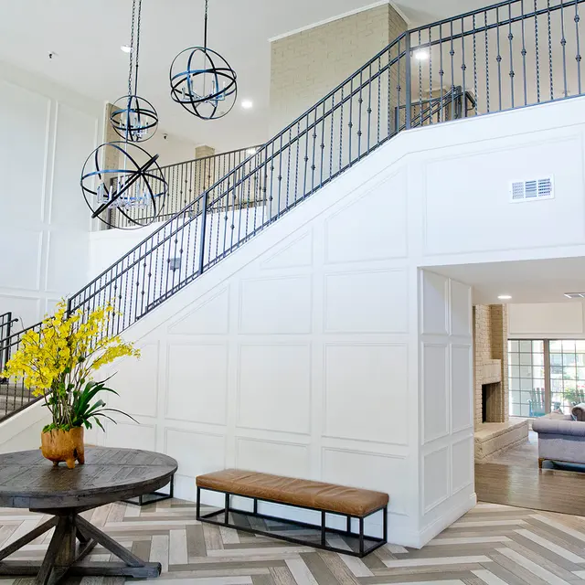 A spacious modern lobby with a staircase, decorative lighting, and a seating area.