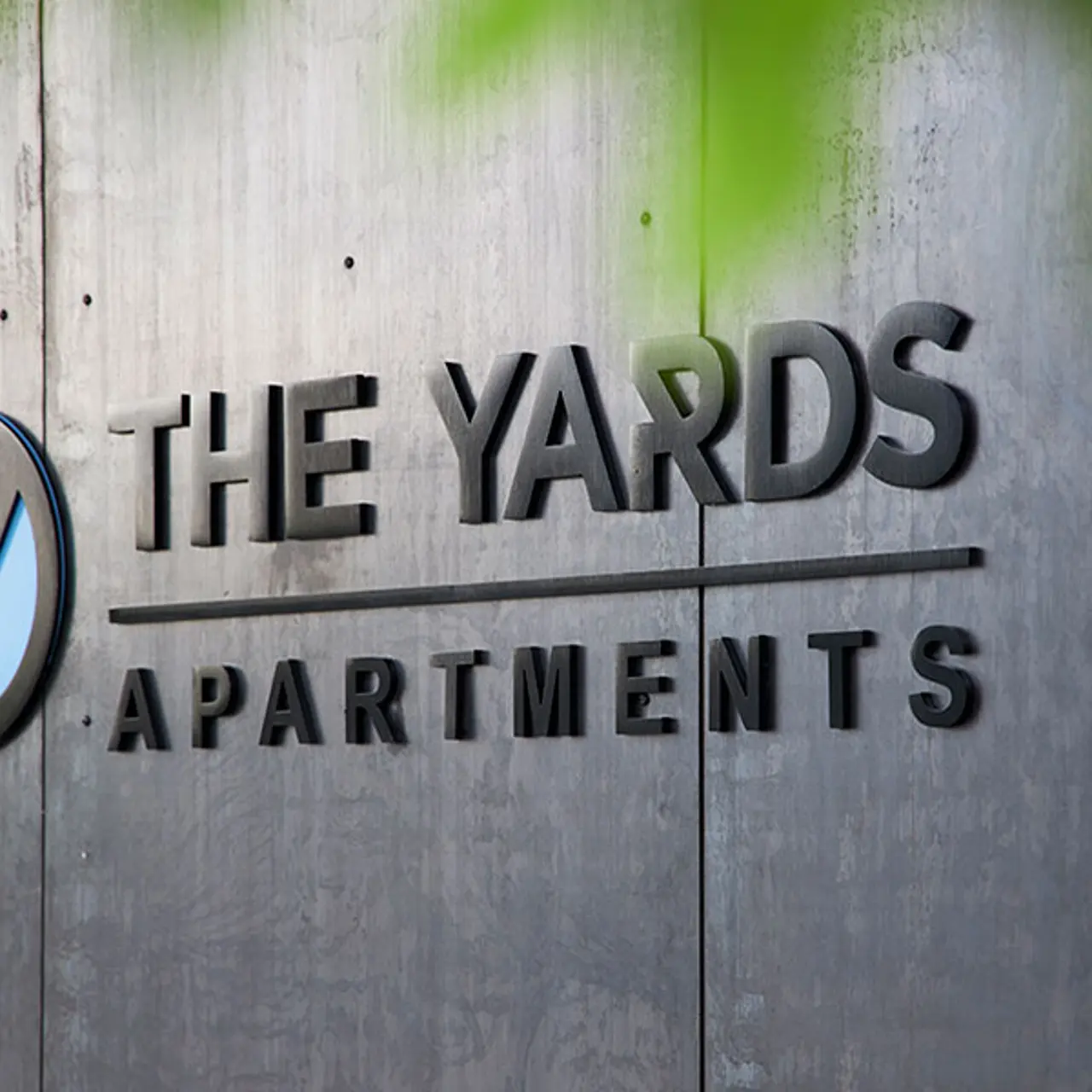 The Yards Apartments Sign Sign for The Yards Apartments featuring a blue and black logo on a concrete wall.