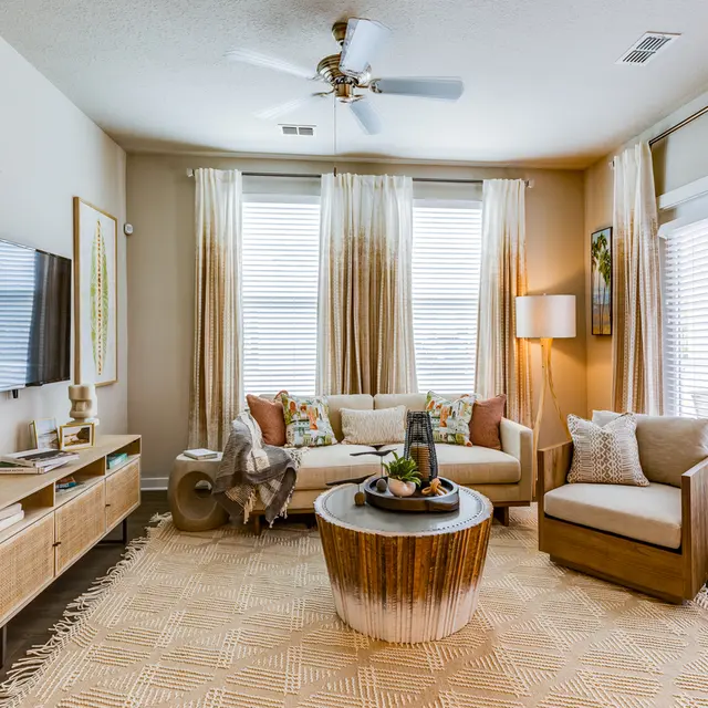 Modern living room with a beige sofa, wooden furniture, a round coffee table, and decorative plants.