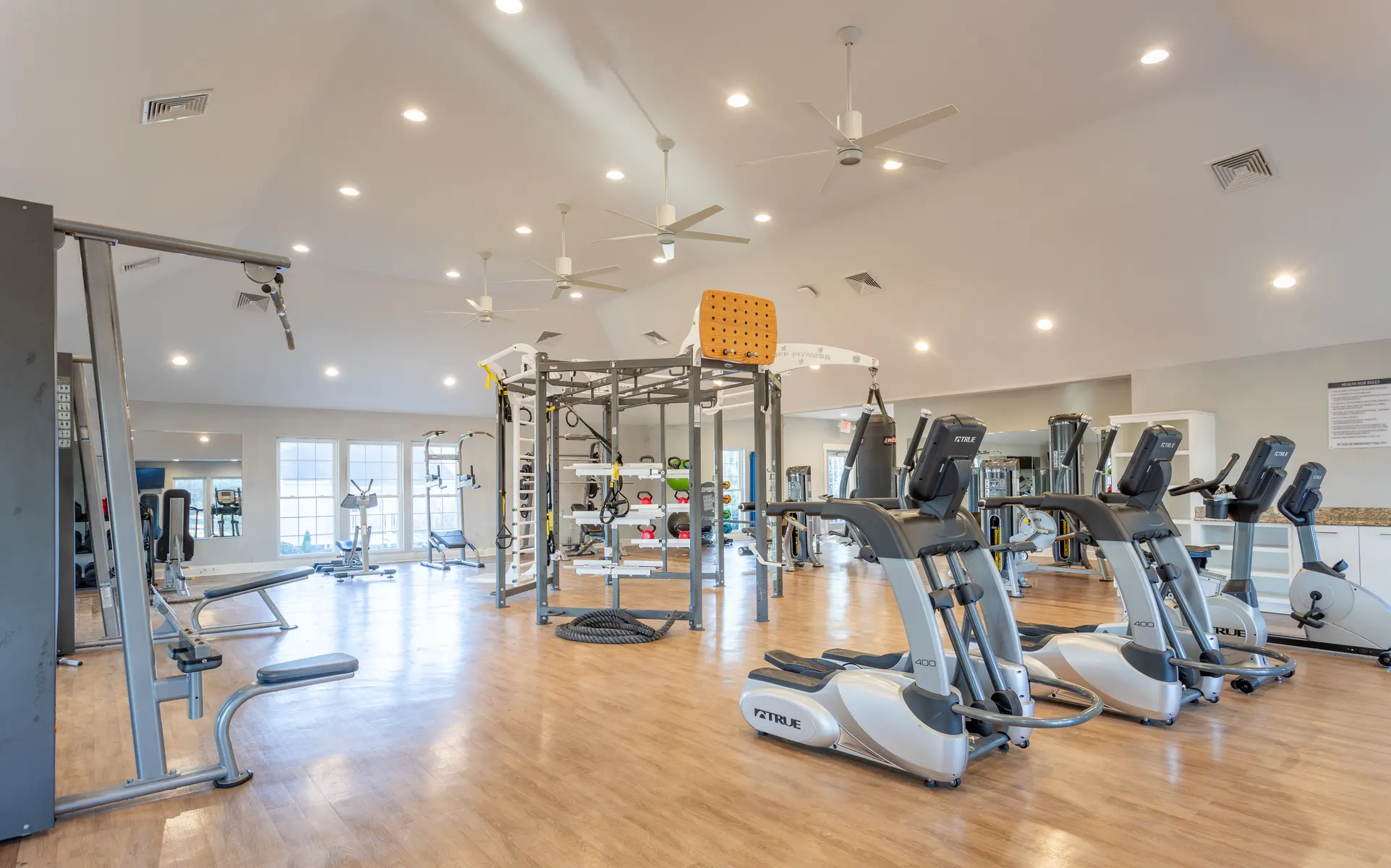 A spacious gym featuring various exercise machines, bright lighting, and a dedicated workout area with equipment.