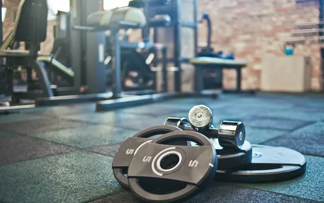 Gym Equipment and Weights A collection of dumbbells and weight plates on a gym floor with exercise equipment in the background.