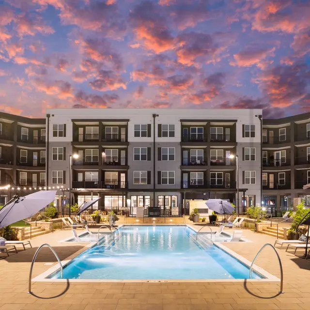 A modern apartment complex featuring a swimming pool at dusk with a colorful sky.