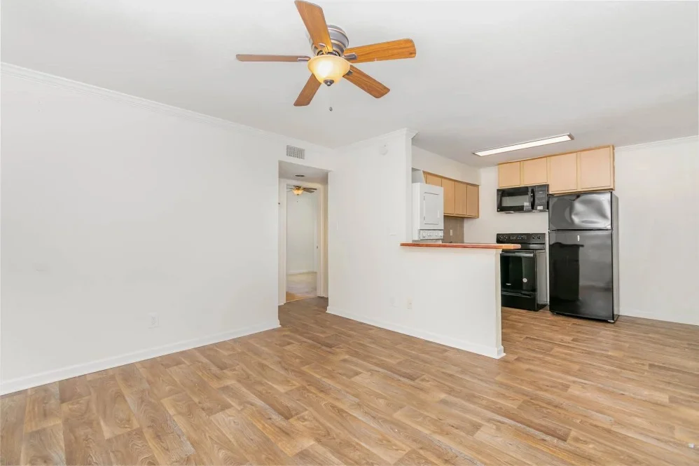 Stylish Apartment Interior An open living area with a ceiling fan, wooden floor, and kitchen appliances visible in the background.