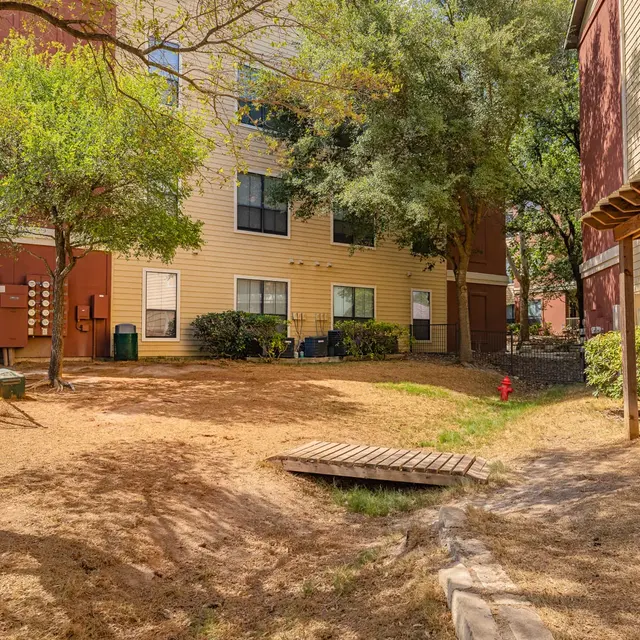 A sunny courtyard area in an apartment complex with grass, trees, and a wooden bridge.