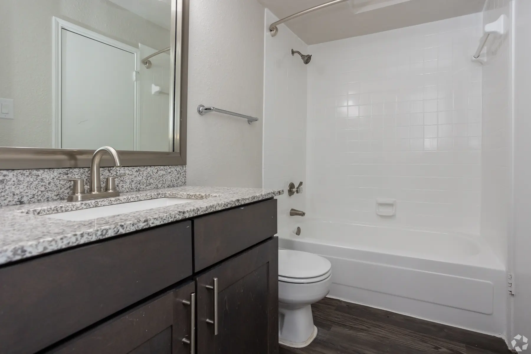 A modern bathroom featuring a sink with a granite countertop, a mirror, and a bathtub with a shower.