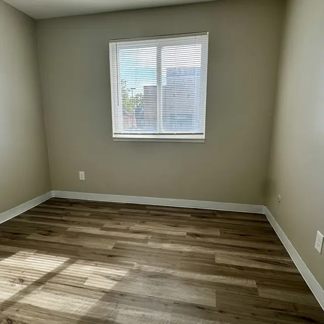 Vacant Room with Natural Light A vacant room with light-colored walls and wooden flooring. A window allows natural light to enter, and there are minimal furnishings.