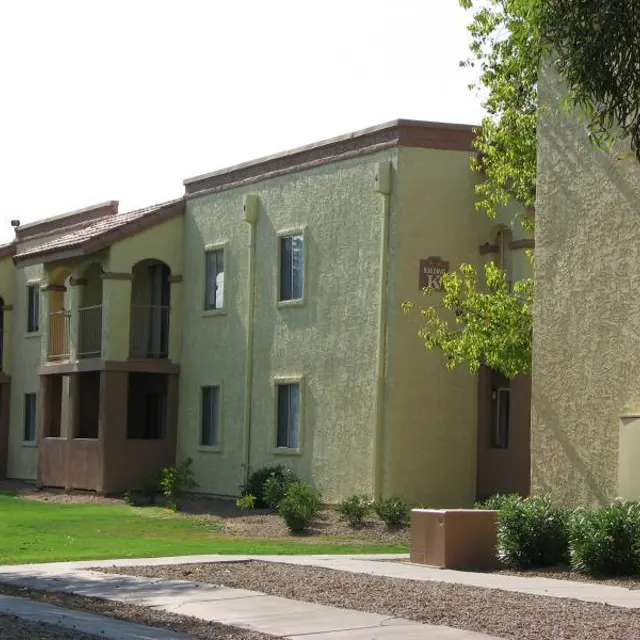 Residential Apartment Complex A row of pale yellow apartment buildings with green grass and trees in front. The architecture features arches and balconies.