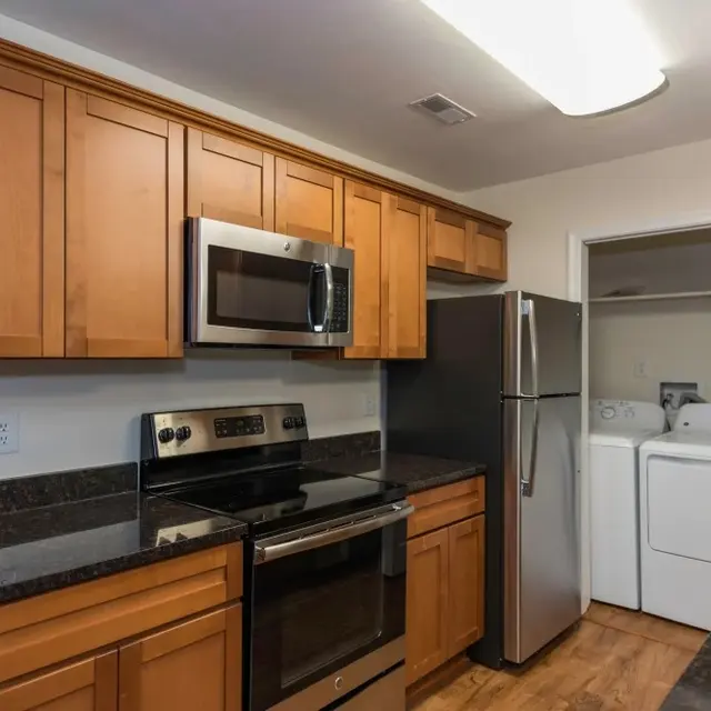 Modern kitchen featuring wooden cabinets, stainless steel appliances, and a laundry area in the background.