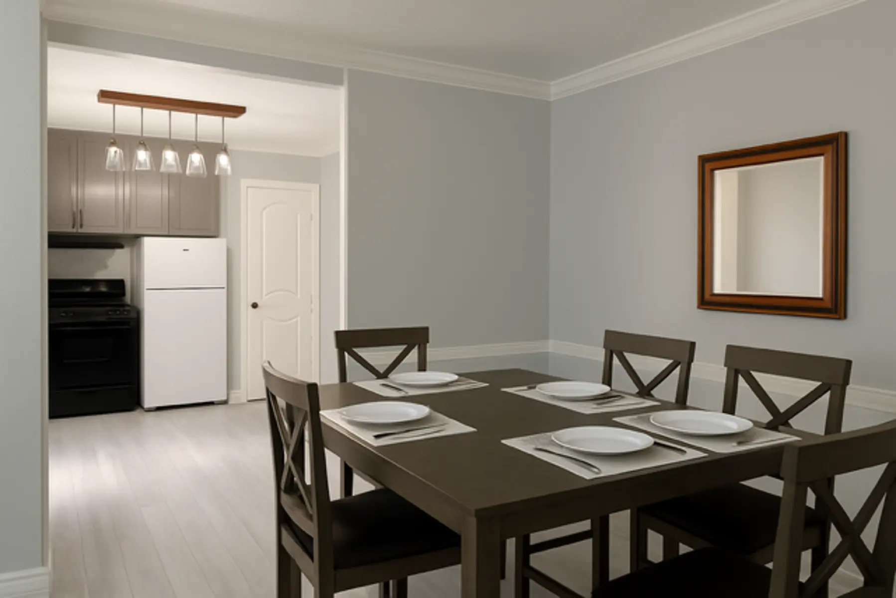 A modern dining area featuring a rectangular table set for six with white plates, surrounded by wooden chairs. The room has light gray walls and a wooden mirror on the wall. A kitchen is visible in the background with black appliances and a light fixture above the table.