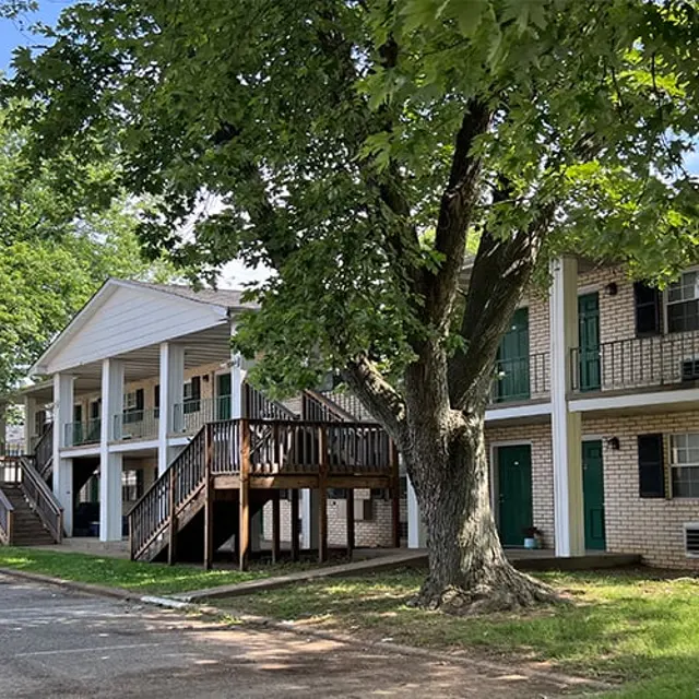Residential Apartment Complex Exterior view of a two-story apartment building surrounded by trees, featuring wooden staircases and balconies.