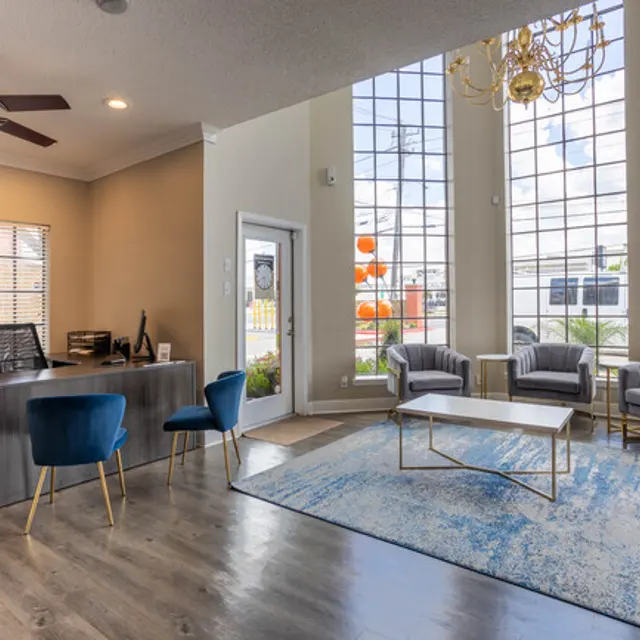 Modern Reception Area A modern reception area featuring a desk with a computer, two blue chairs, and a lounge area with gray armchairs and a coffee table. Large windows let in natural light, showcasing an outdoor view with orange decorations.