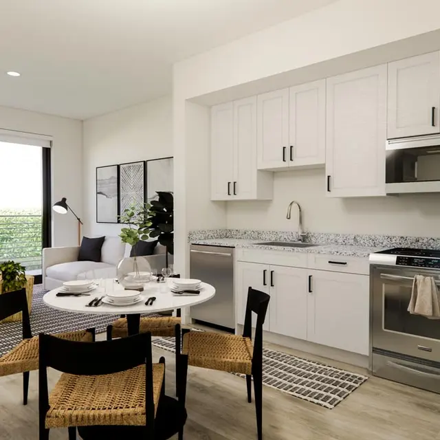 A modern kitchen featuring white cabinets, a stainless steel stove, microwave, and a dining table with black chairs. Natural light comes through large windows with greenery visible outside.