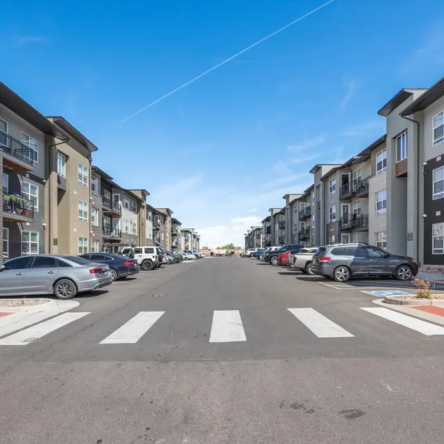 View of a residential street lined with modern apartment buildings and parked cars.