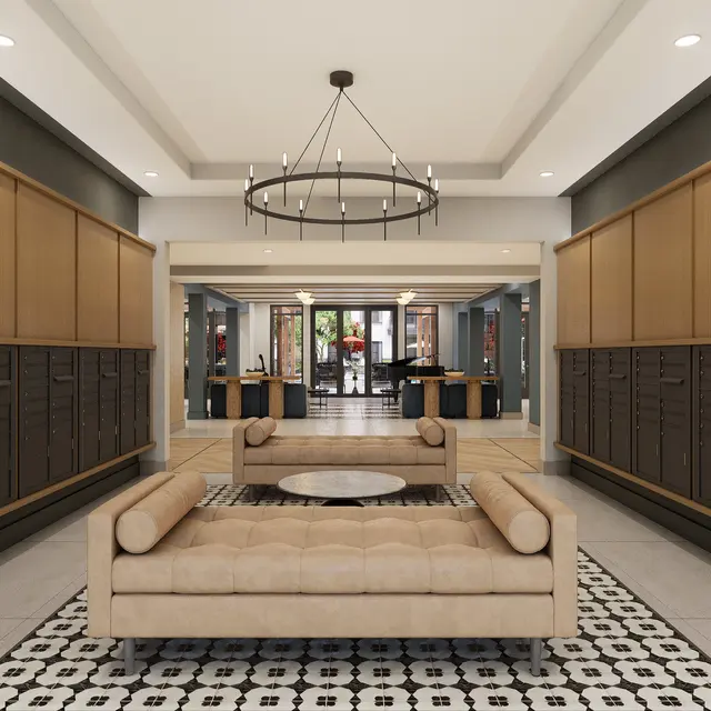 A modern lobby interior featuring a spacious layout with a beige sofa and circular coffee table on a patterned rug. Dark cabinetry lines the walls, and a chandelier hangs from the ceiling. The space is well-lit and inviting with mirrors reflecting the area.