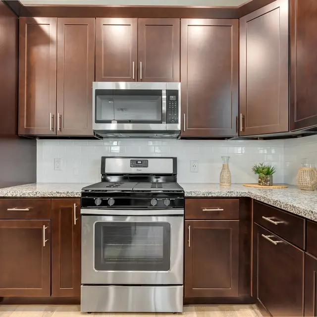 A modern kitchen featuring dark wooden cabinets, a silver stove, a microwave, and a granite countertop with minimal decor.
