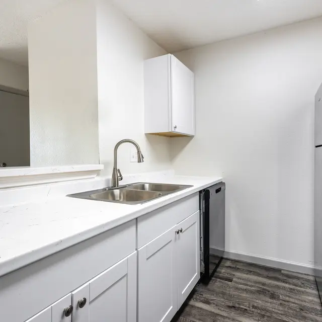 A clean and modern kitchen featuring white cabinetry, a sink, a dark refrigerator, and laminate flooring.