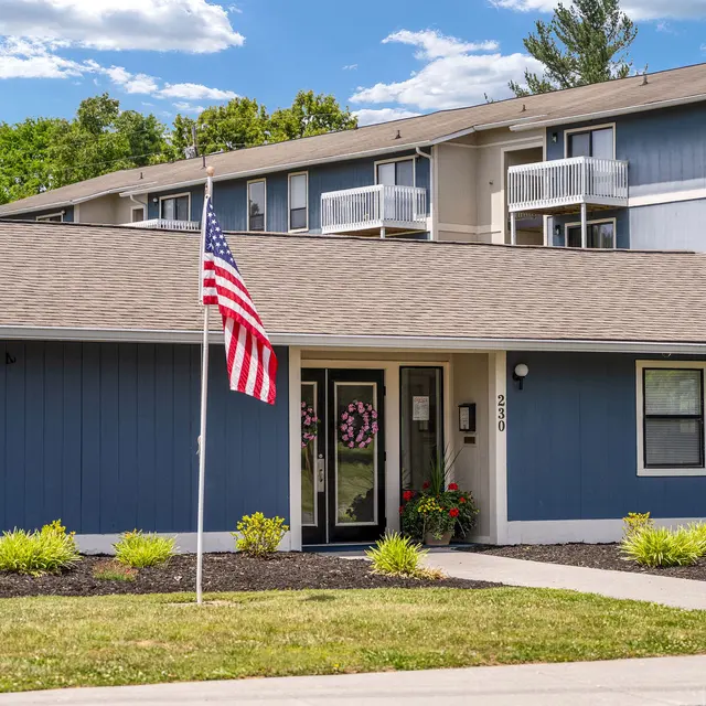 A blue building with a front entrance and American flag in front, surrounded by greenery.