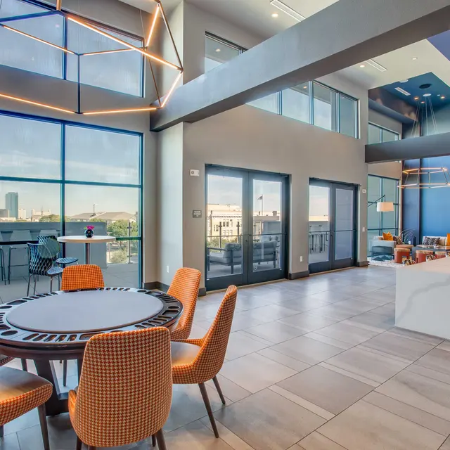 An indoor modern living space featuring a circular dining table with colorful chairs, large windows, and modern decor elements including sleek lighting fixtures and a stylish dining area.
