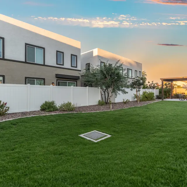 Modern Townhouse Exterior at Sunset A view of modern townhouses surrounded by a green lawn and a white fence, under a colorful sunset sky.