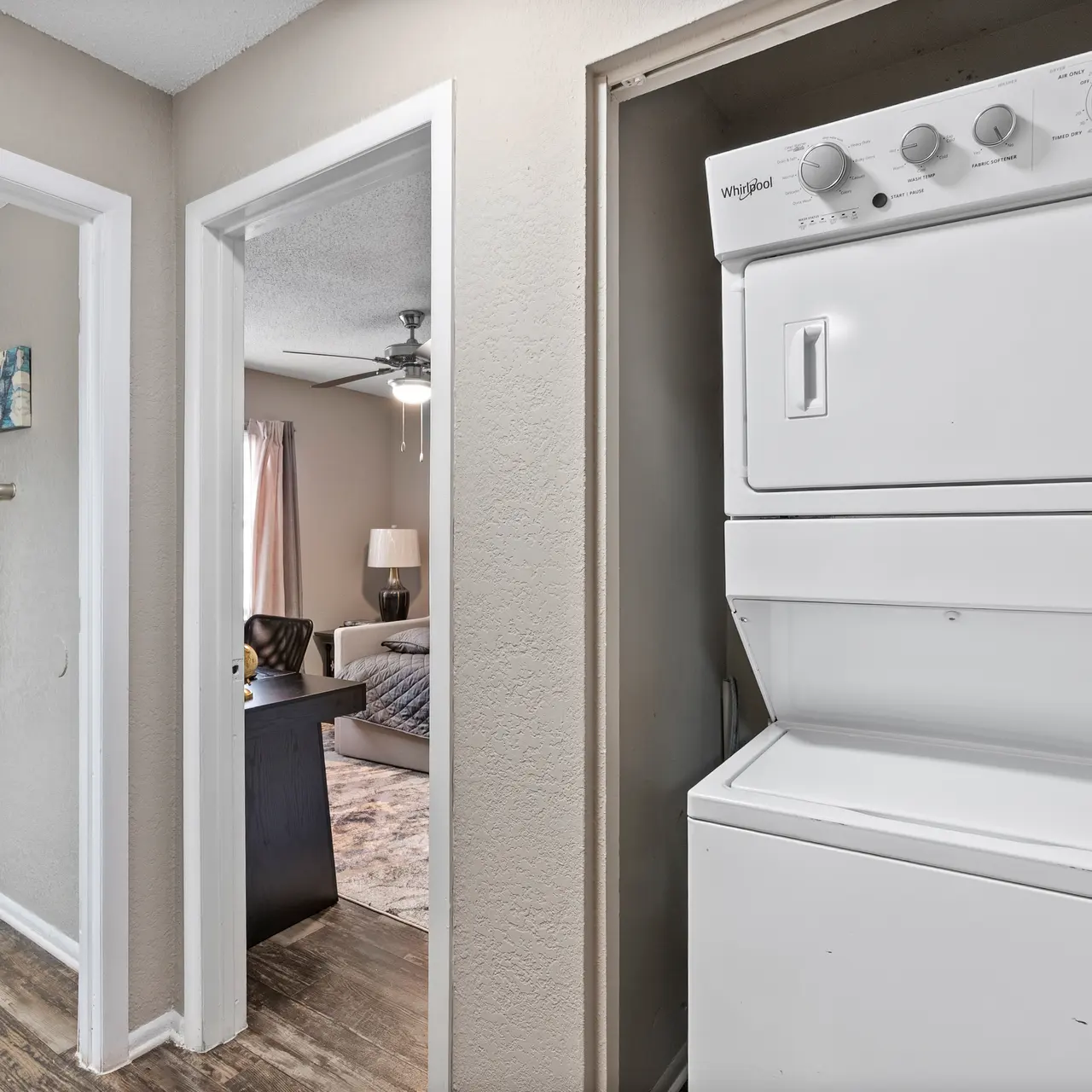 View of a laundry unit in a small hallway, with a bathroom visible on the left and a living area in the background.