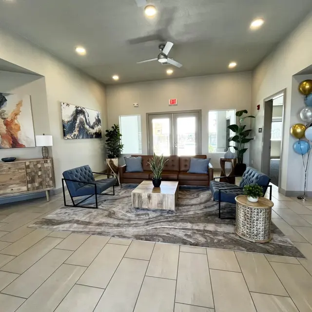 Modern Lobby Design A modern lobby featuring a seating area with two blue chairs, a brown couch, and a light wooden coffee table. The space is adorned with decorative plants, lamps, and artwork on the walls. There are balloons in various colors by the entrance and large windows allowing natural light.