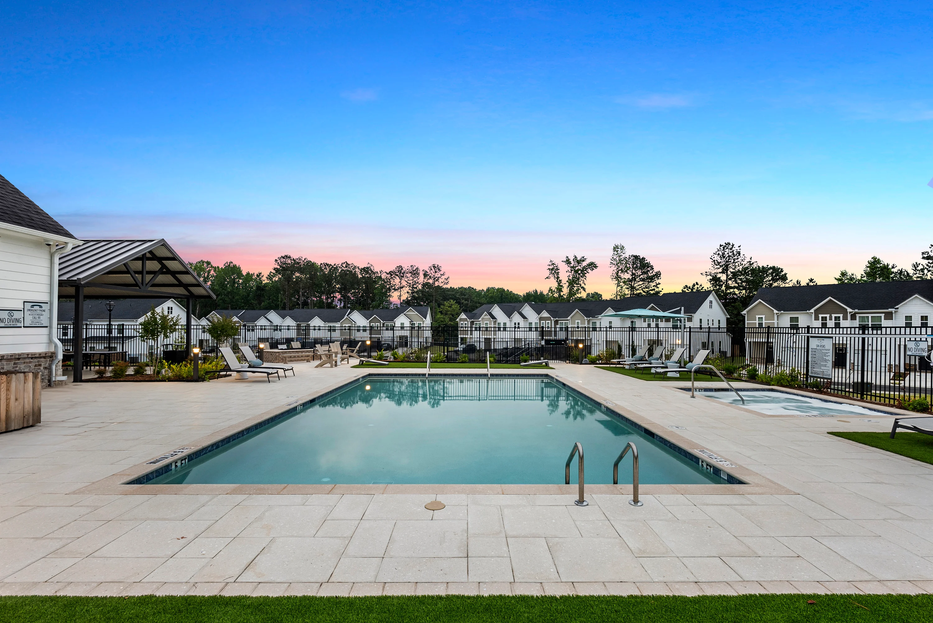 Community Pool Area at Sunset A beautiful pool area with lounge chairs and a surrounding fence, set against a backdrop of homes during sunset.