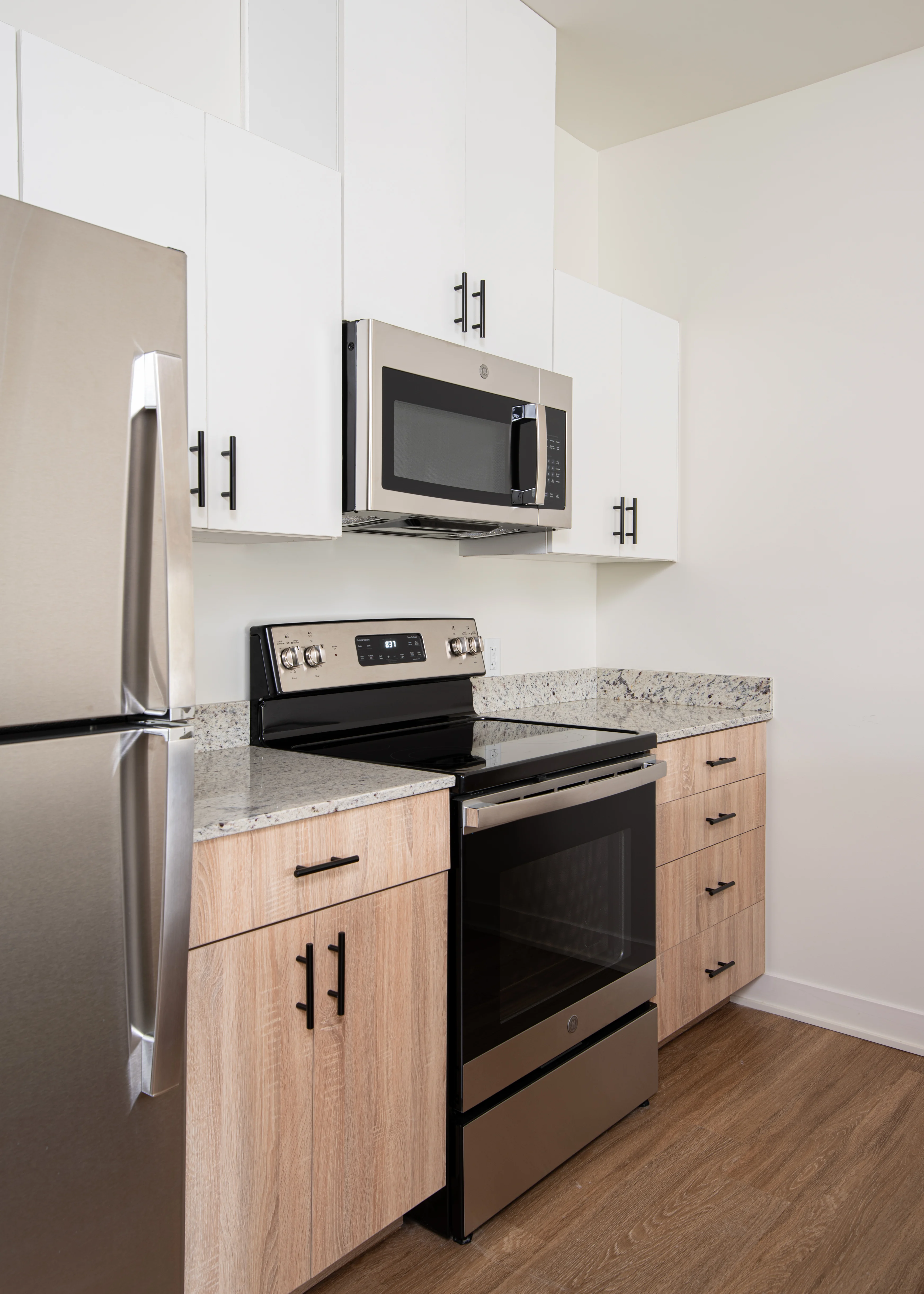 A modern kitchen featuring an integrated stainless steel refrigerator, a microwave above a black stove, and wooden cabinets with a light-colored countertop.
