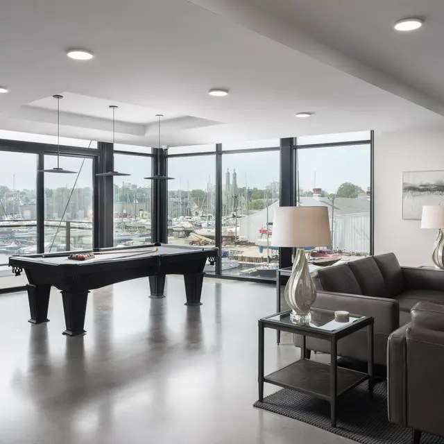 Spacious modern living area featuring a billiards table, large windows with views of a harbor, comfortable seating, and stylish decor.