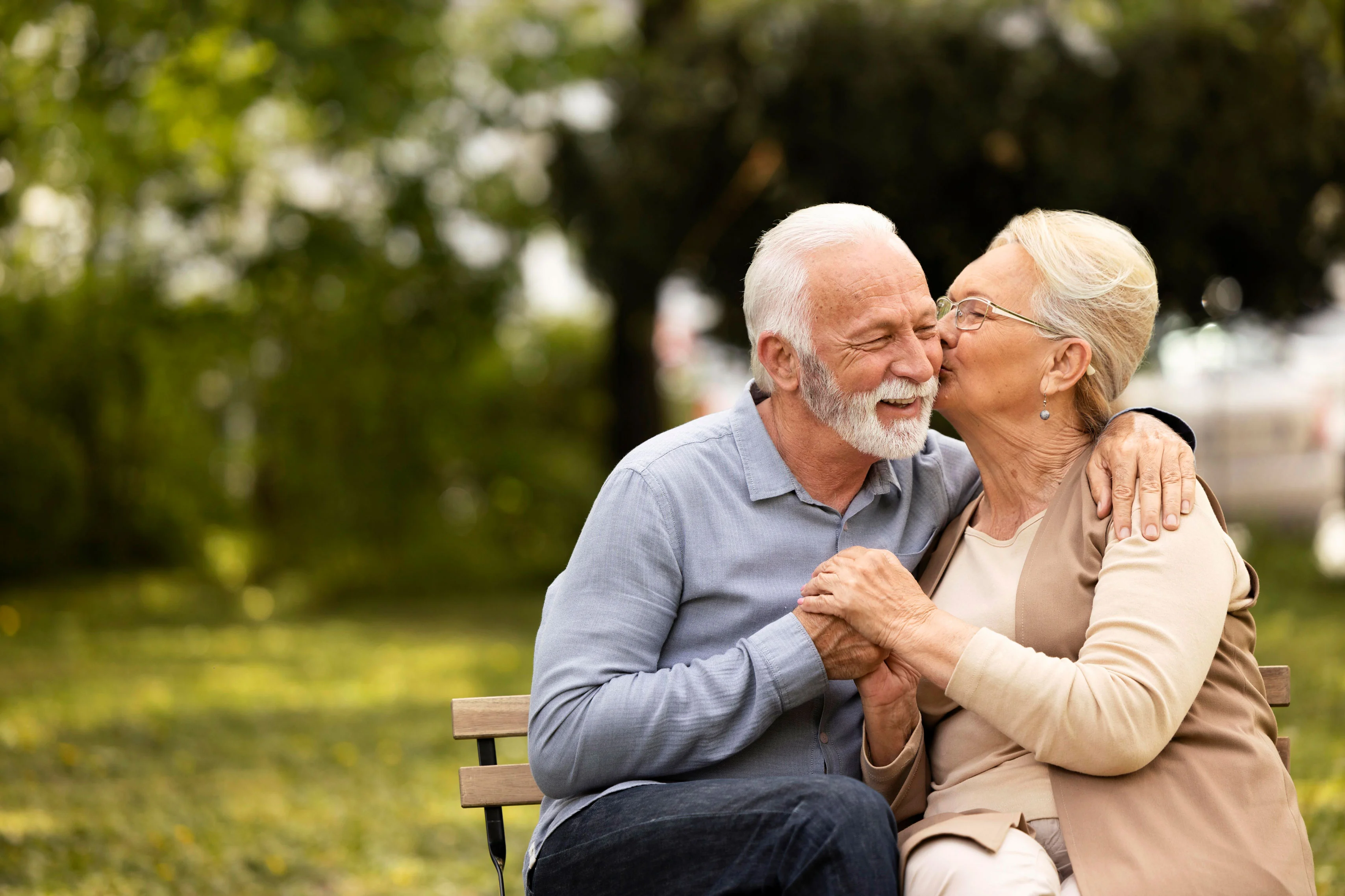 Elderly Couple in Love An elderly couple sitting on a park bench, smiling and sharing a tender moment as one kisses the other on the cheek.