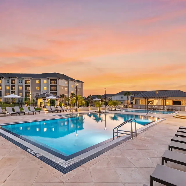 Luxury Apartment Pool Area at Sunset A beautiful pool area at a luxury apartment complex during sunset, featuring lounge chairs and surrounding buildings.