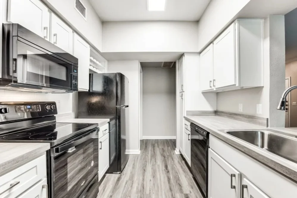 A modern kitchen featuring stainless steel appliances, black and white cabinetry, and sleek countertops. The kitchen has an open layout leading to a hallway.