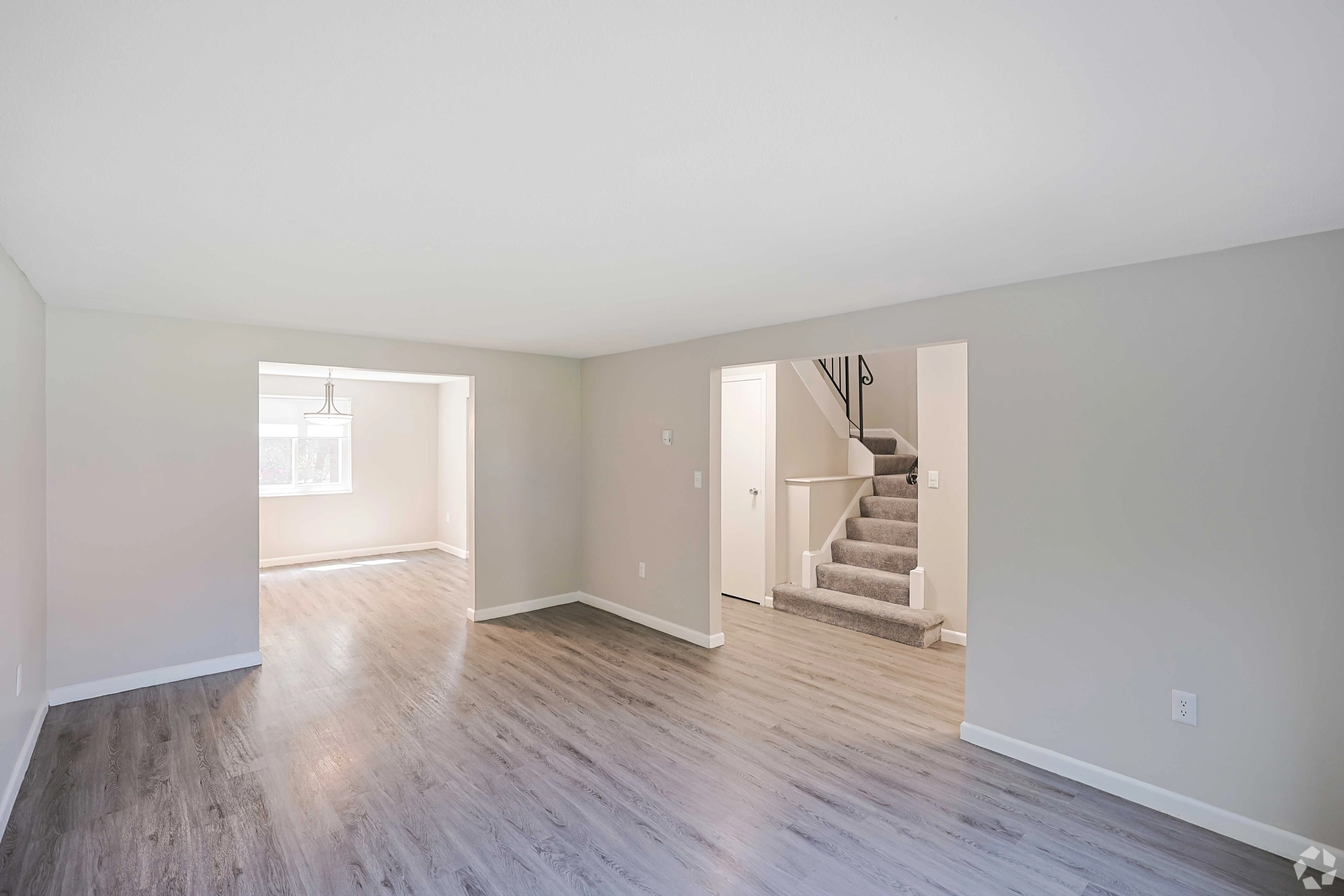 Spacious Living Area A spacious, light-filled living area featuring light-colored walls and flooring. There are doorways leading to another room and stairs. Natural light streams in through a window, enhancing the open feel of the space.