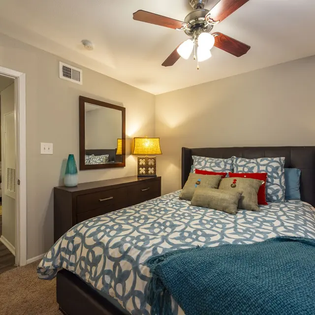 Cozy bedroom featuring a bed with decorative pillows, two nightstands with lamps, and a ceiling fan. Wall mirror included.