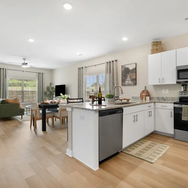 A bright, modern kitchen and dining area featuring white cabinetry, stainless steel appliances, and a wooden dining table with multiple chairs.