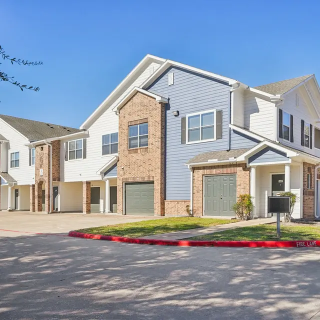 A contemporary residential apartment complex featuring several buildings with a mix of brick and siding exteriors, set against a clear blue sky.
