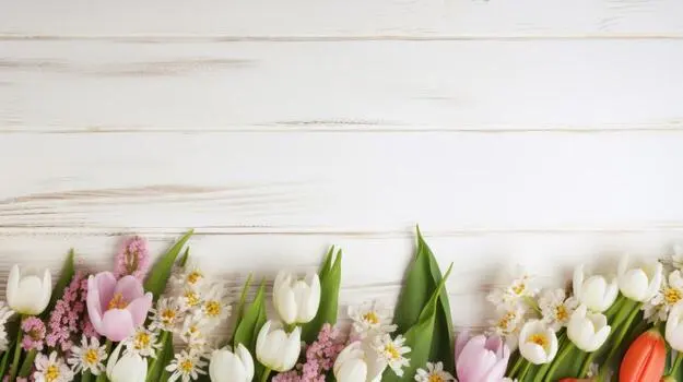 A beautiful arrangement of spring flowers including tulips and daisies on a white wooden background.