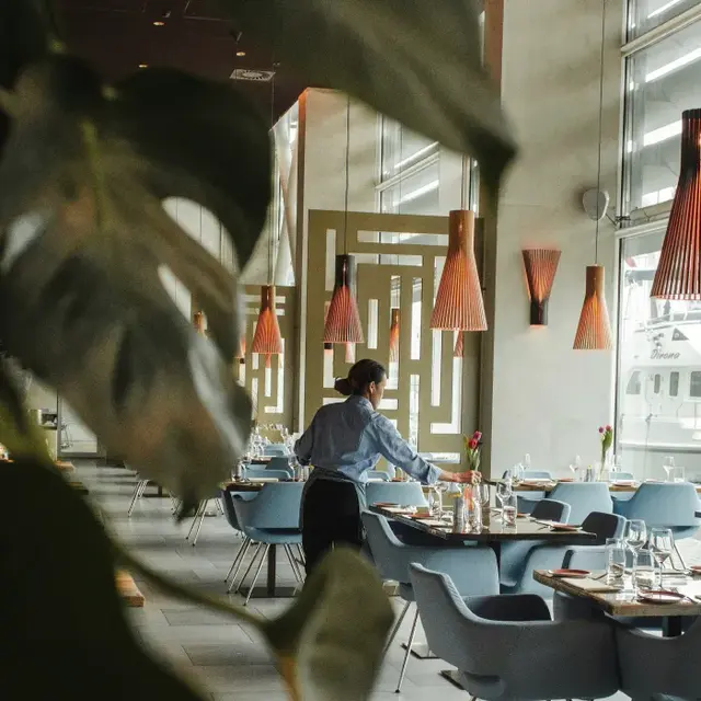 Contemporary Restaurant Interior A waiter arranging tables in a modern restaurant with stylish decor, featuring pendant lights and large windows.