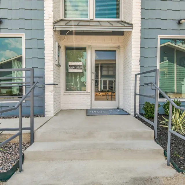 Entrance of a modern building with a ramp and railing, decorated with plants and colorful flowers.