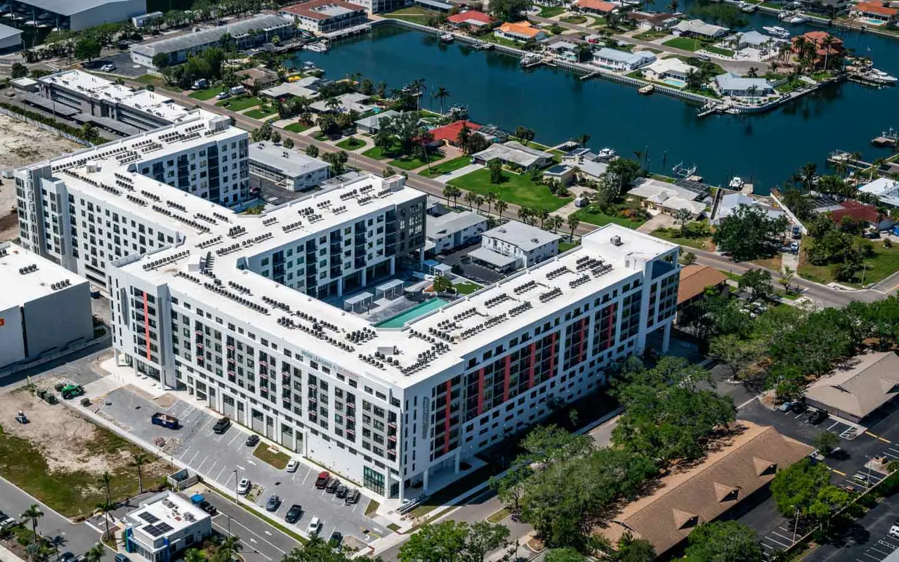 Aerial view of a modern apartment complex with swimming pool, surrounded by greenery and a waterway in the background.