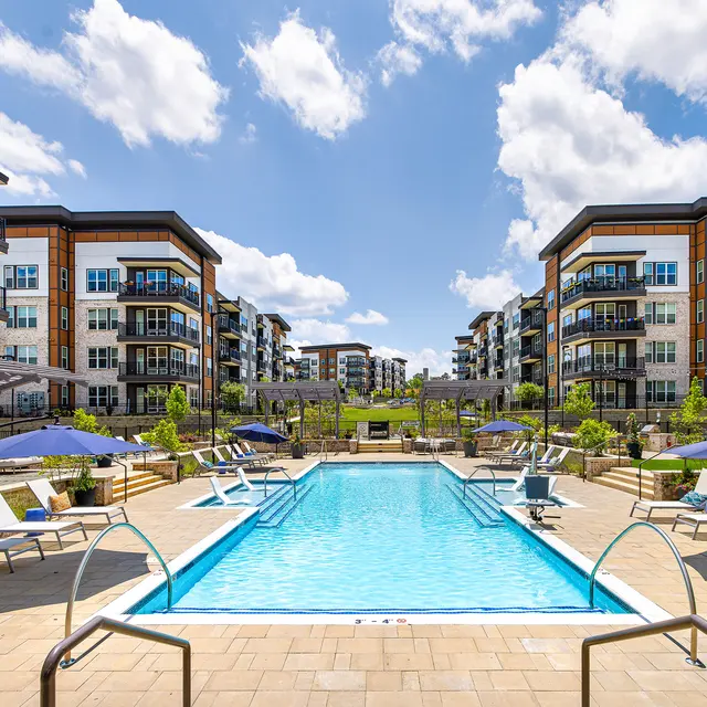 Outdoor pool area surrounded by modern apartment buildings with palm trees and lounge chairs.