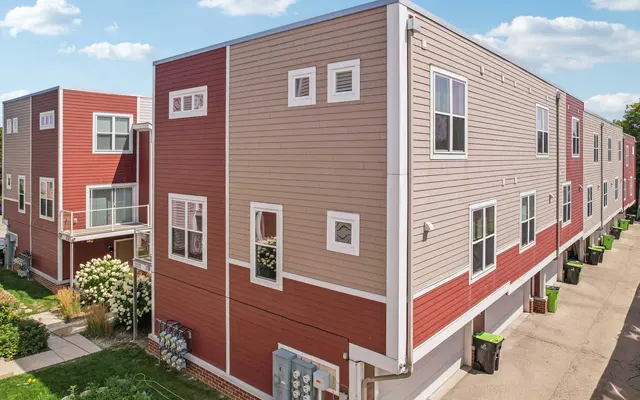 View of a modern apartment complex with a mix of red and beige siding, featuring several windows and a paved walkway.