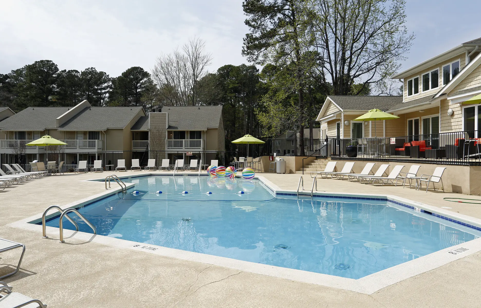 View of a swimming pool surrounded by lounge chairs and umbrellas, with a residential building in the background.