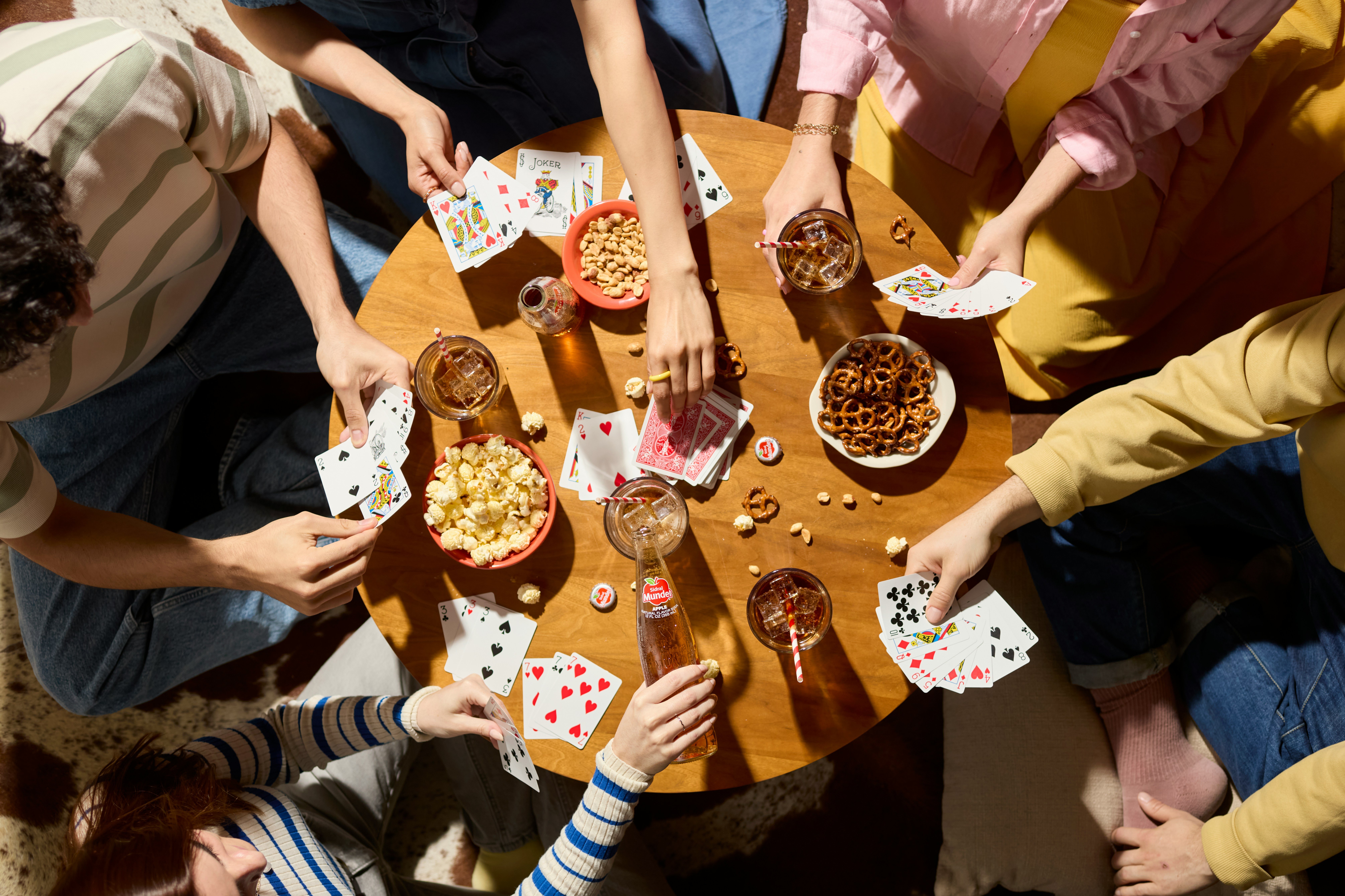 A group of friends gathered around a table playing cards, with snacks like popcorn and pretzels around them, creating a social atmosphere.