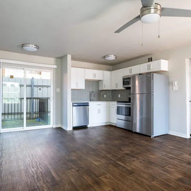 Modern kitchen and living area with wood flooring, white cabinets, and stainless steel appliances.