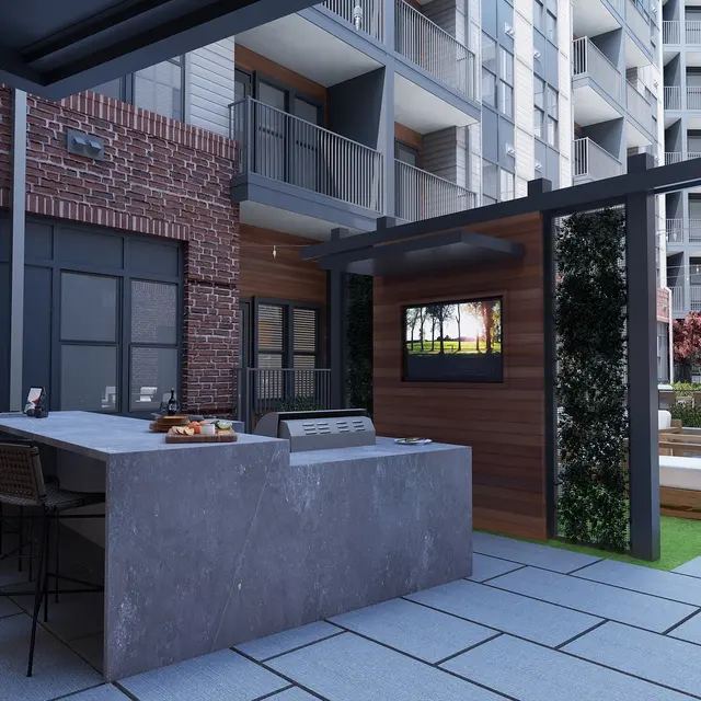 A modern outdoor lounge area featuring a bar with seating, a TV on a wooden panel, and comfortable seating surrounded by greenery.