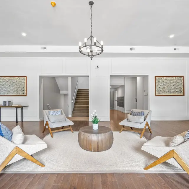 A modern living room featuring stylish chairs and a round wooden coffee table on a rug, with artwork on the walls and a chandelier hanging from the ceiling.