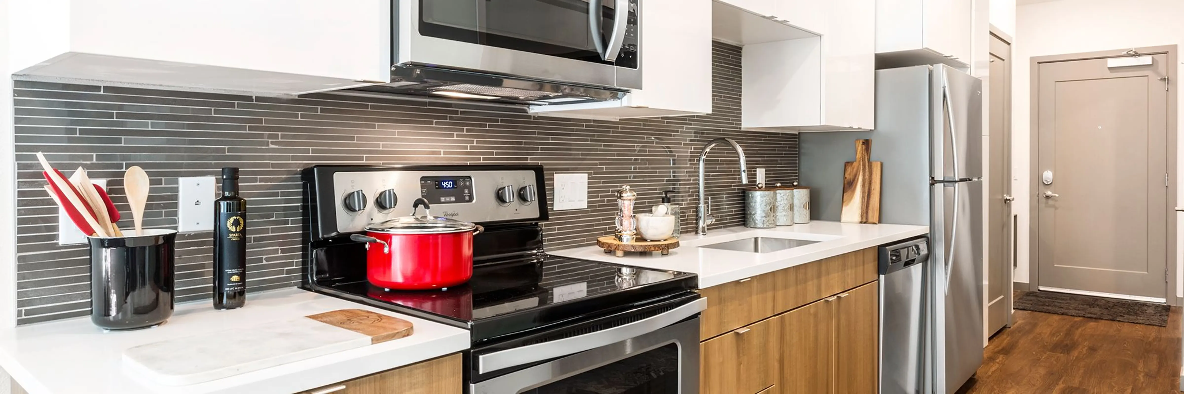 Modern Kitchen Design A modern kitchen featuring stainless steel appliances, wooden cabinets, and a marble countertop with a red pot on the stove.