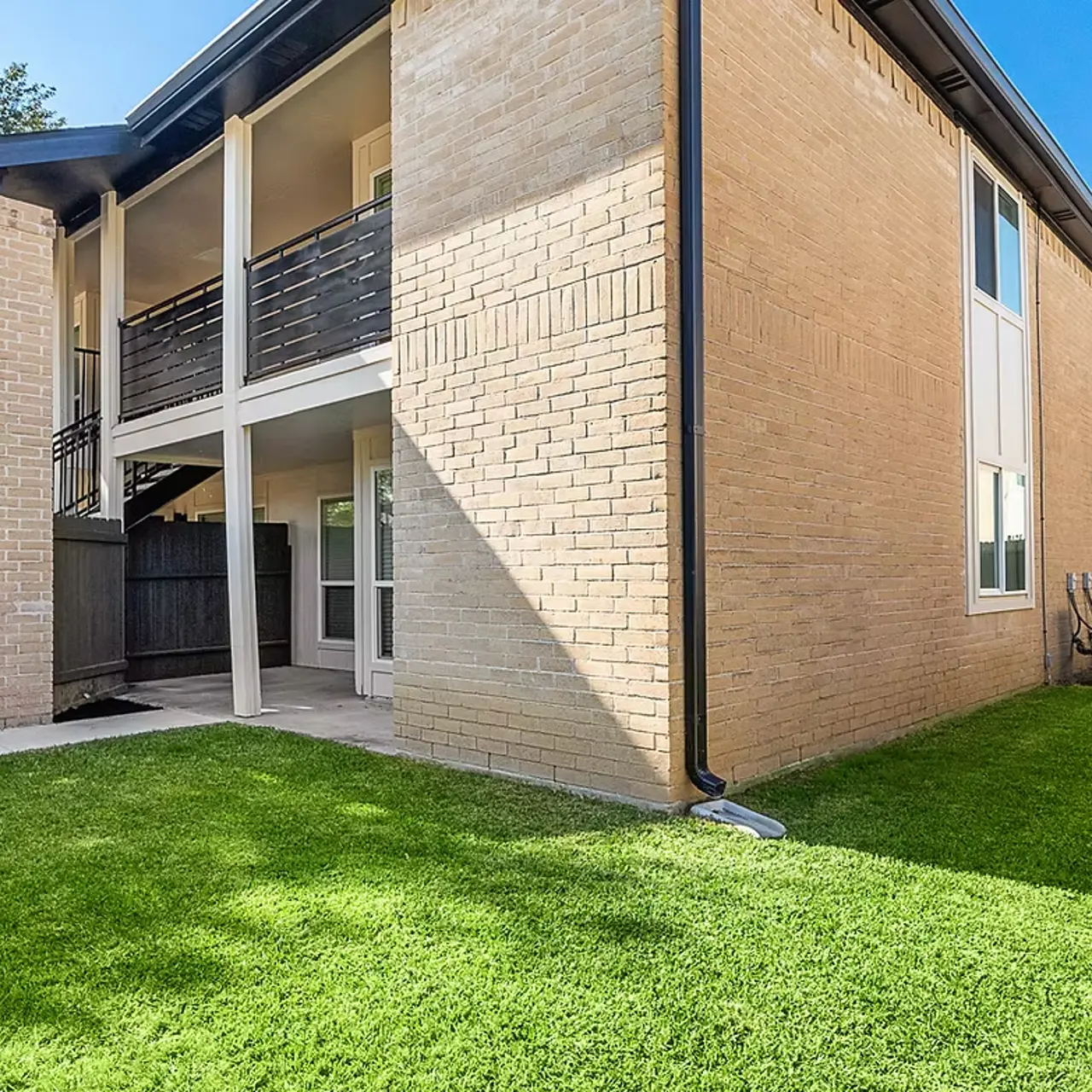 Exterior view of a modern apartment with green lawn and fenced backyard