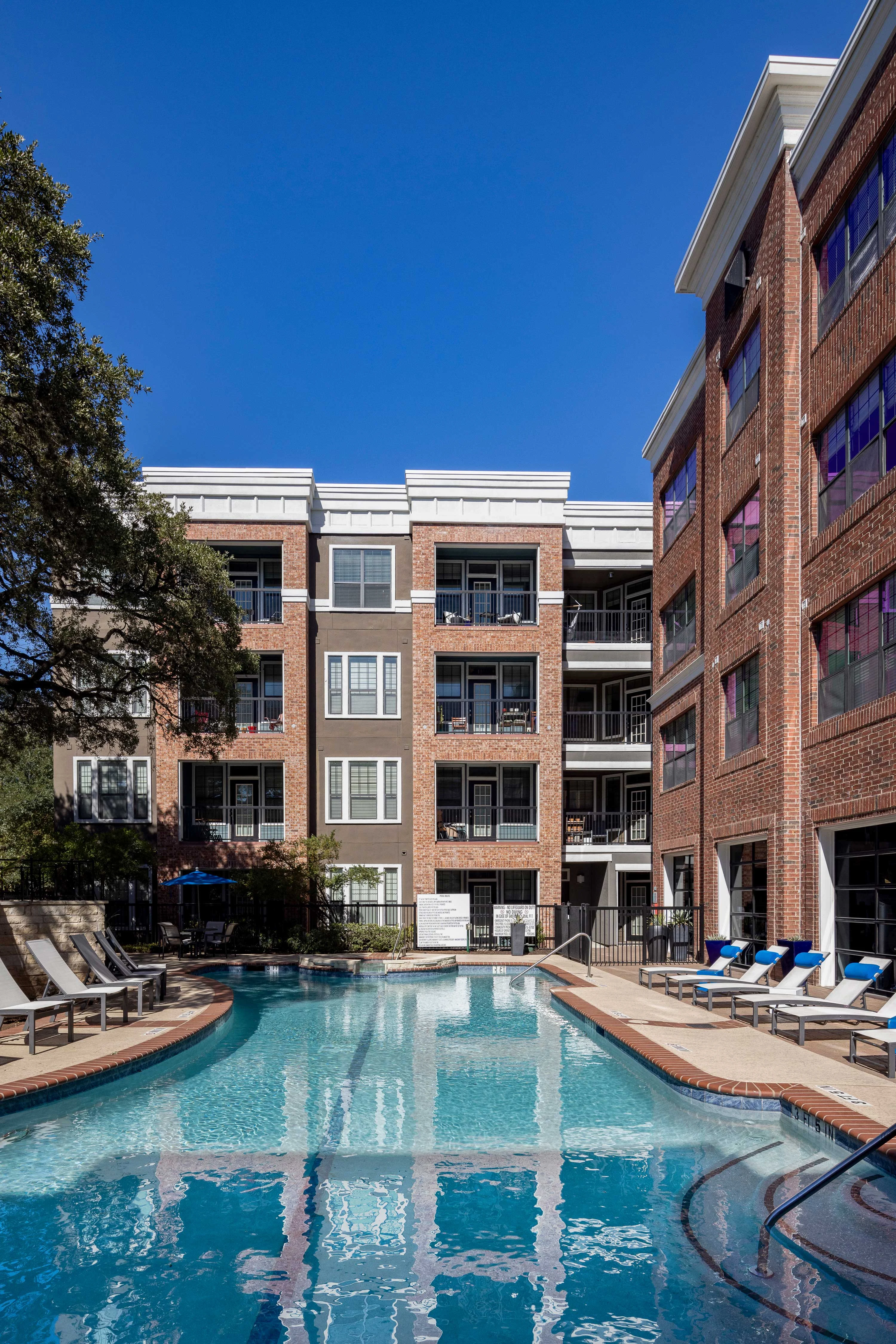Apartment Complex Pool Area A modern apartment complex featuring a swimming pool surrounded by lounge chairs, with buildings in the background under a clear blue sky.